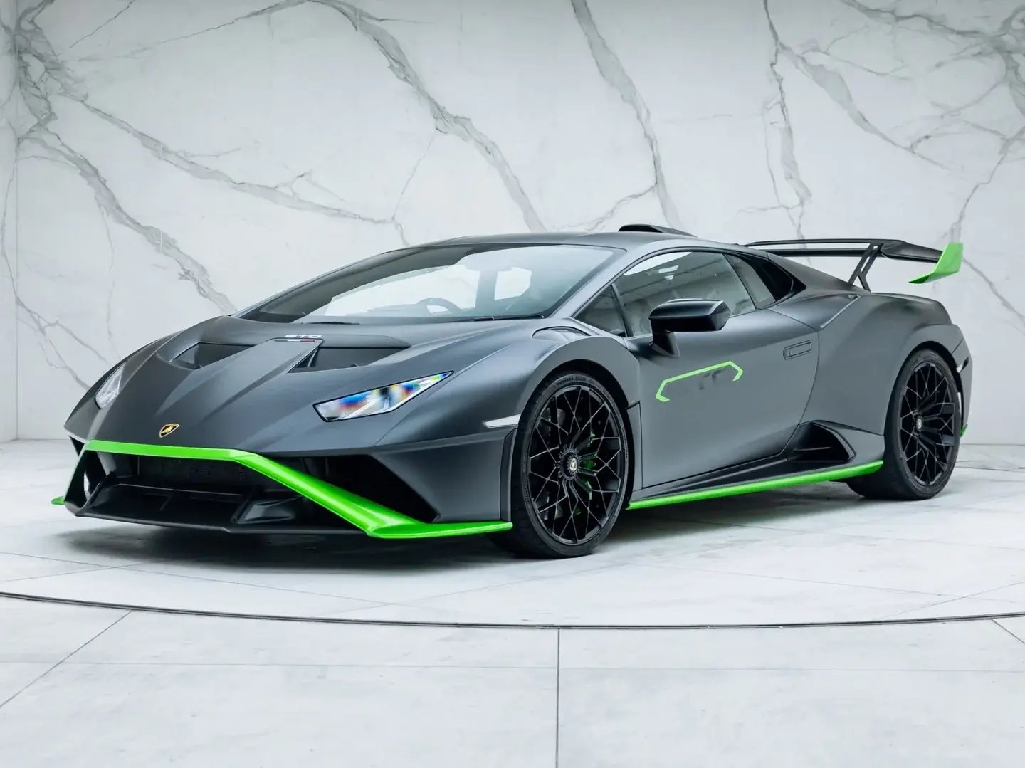 Grey Lamborghini Huracán STO with green accents, front three-quarter view in a showroom