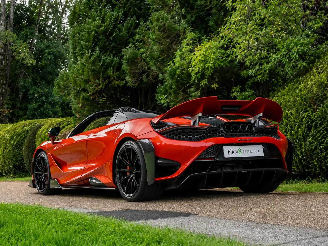 Orange McLaren 675LT Spider, rear three-quarter, on a country road.